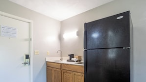A kitchen with a black refrigerator, wooden cabinets, a white countertop, and a sink.