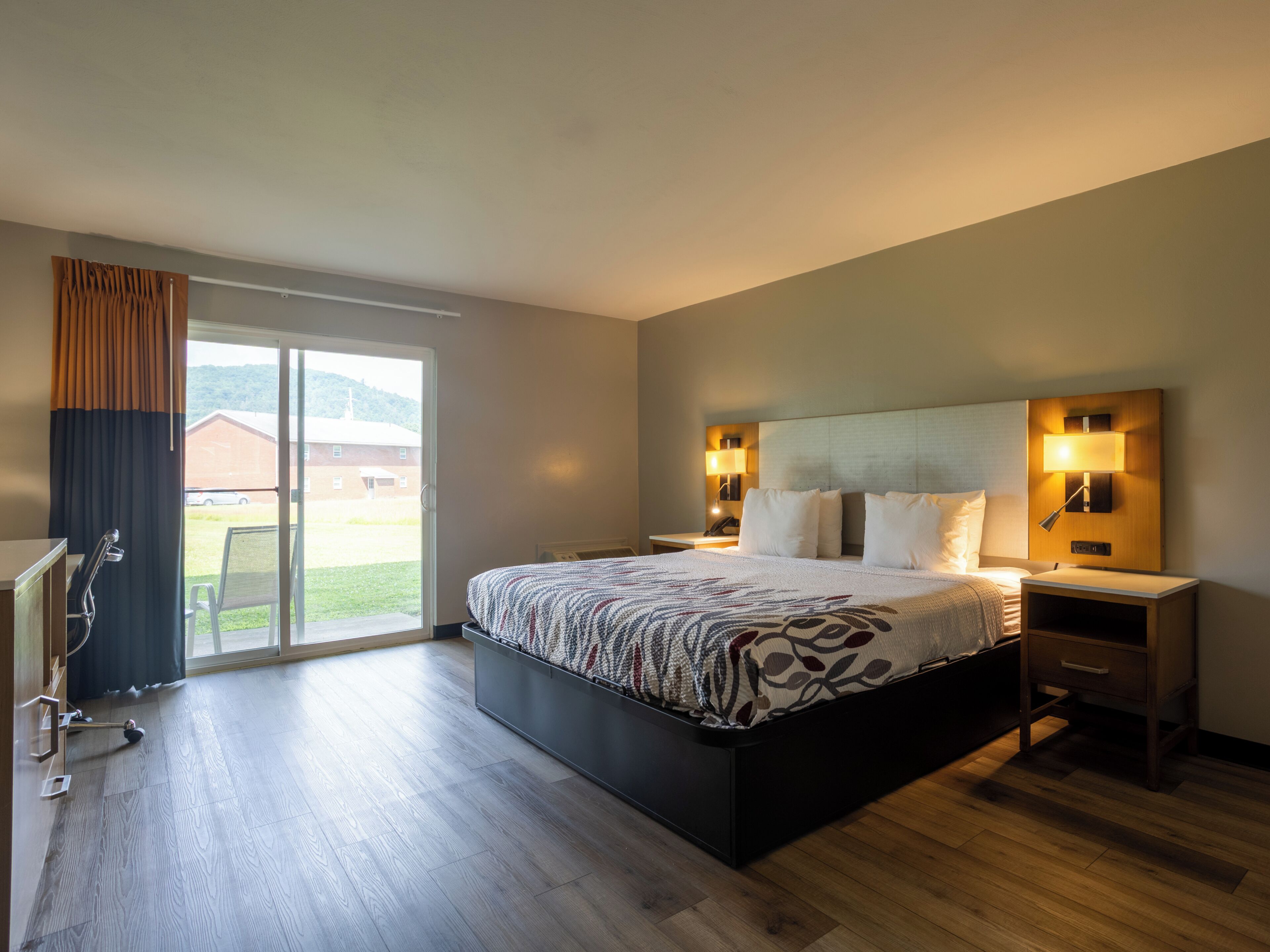 A hotel room with a large bed, a desk, a chair, and a view of the outdoors.
