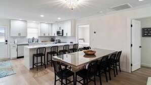 Une cuisine moderne avec des meubles blancs, un îlot central doté de chaises noires et un lustre.