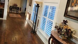 A hallway with wooden flooring, a decorative table with flowers, and a window with blinds. - Newly Renovated Private Ranch Get-A-Way (Pilot Point)