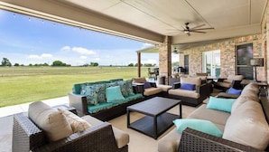 An outdoor patio with wicker furniture, a brick wall, and a view of a grassy field. - Newly Renovated Private Ranch Get-A-Way (Pilot Point)