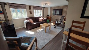 A living room with a sofa, a rocking chair, a coffee table, and a TV mounted on the wall. - Former showhome with indoor pool & gym (Oakhill)