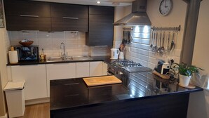 A modern kitchen with dark cabinets, a black countertop, a stove, and a sink. - Former showhome with indoor pool & gym (Oakhill)