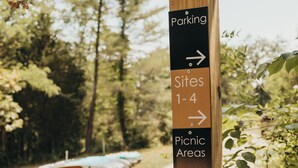 Ein hölzernes Wegweiser mit Pfeilen, die zu verschiedenen Einrichtungen wie Parkplätzen, Picknickbereichen und einem Badehaus zeigen.