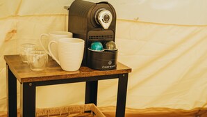 Ein kleiner Holztisch mit einer Kaffeemaschine, einem Korb und einigen Tassen und Gläsern.