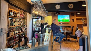 A bar area with shelves of liquor bottles, a bar counter, and a television screen displaying a sports game. - The Vale Hotel (Swindon)