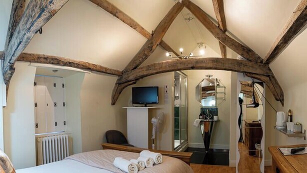 A bedroom with exposed wooden beams, a bed with neatly folded towels, a television, and a radiator. - The Vale Hotel (Swindon)