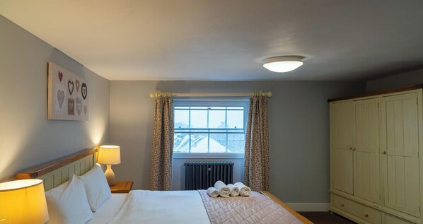 Une chambre d’hôtel avec un lit, deux lampes de chevet, une fenêtre avec des rideaux, un radiateur et une armoire.