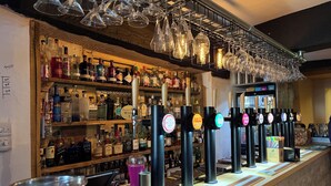 A bar area with multiple liquor bottles, a tap system, and hanging wine glasses. - The Vale Hotel (Swindon)