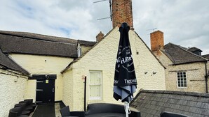 A courtyard with outdoor seating, a black umbrella, and a brick chimney. - The Vale Hotel (Swindon)