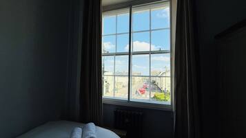 A hotel room with a large window, a bed with white linens, and a radiator below the window.