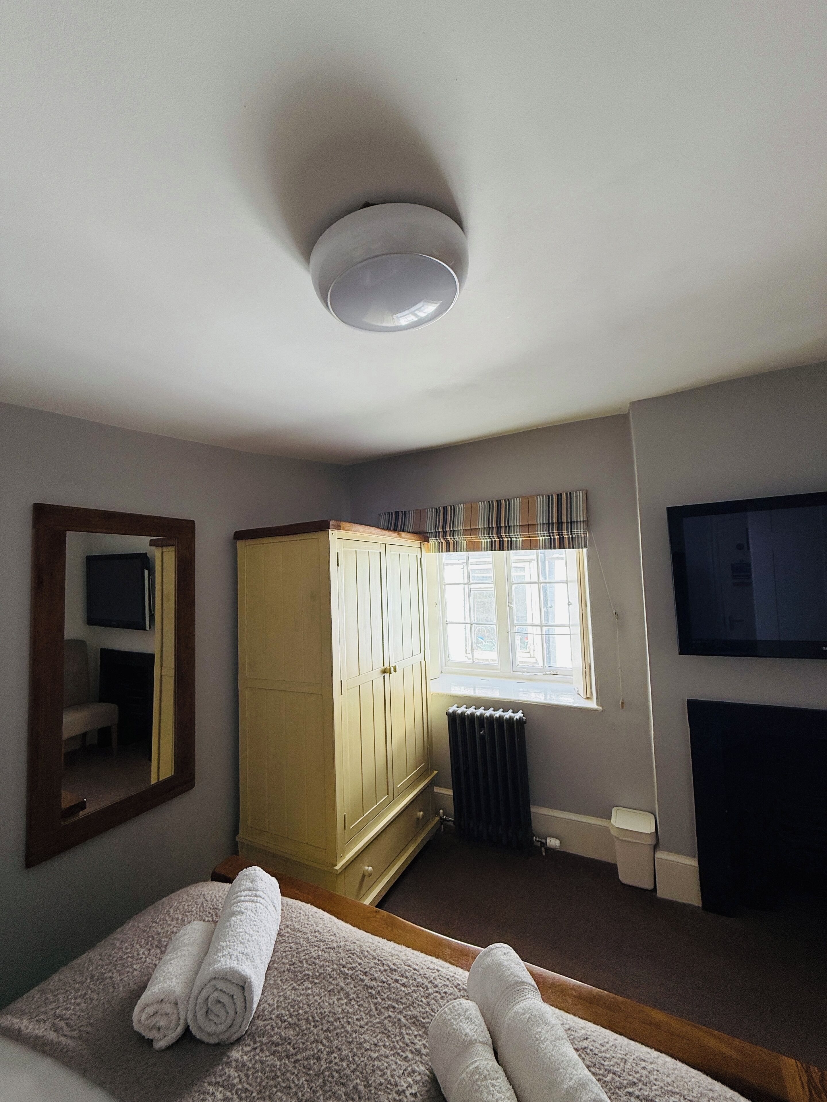 A hotel room with a bed, a wardrobe, a radiator, a television, and a window.