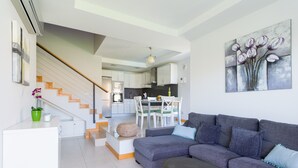 Una sala de estar moderna con un sofá seccional gris, una pequeña mesa redonda y una escalera que lleva a una zona de cocina.