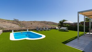 Un área de piscina con césped artificial, sillas de descanso y una pérgola.