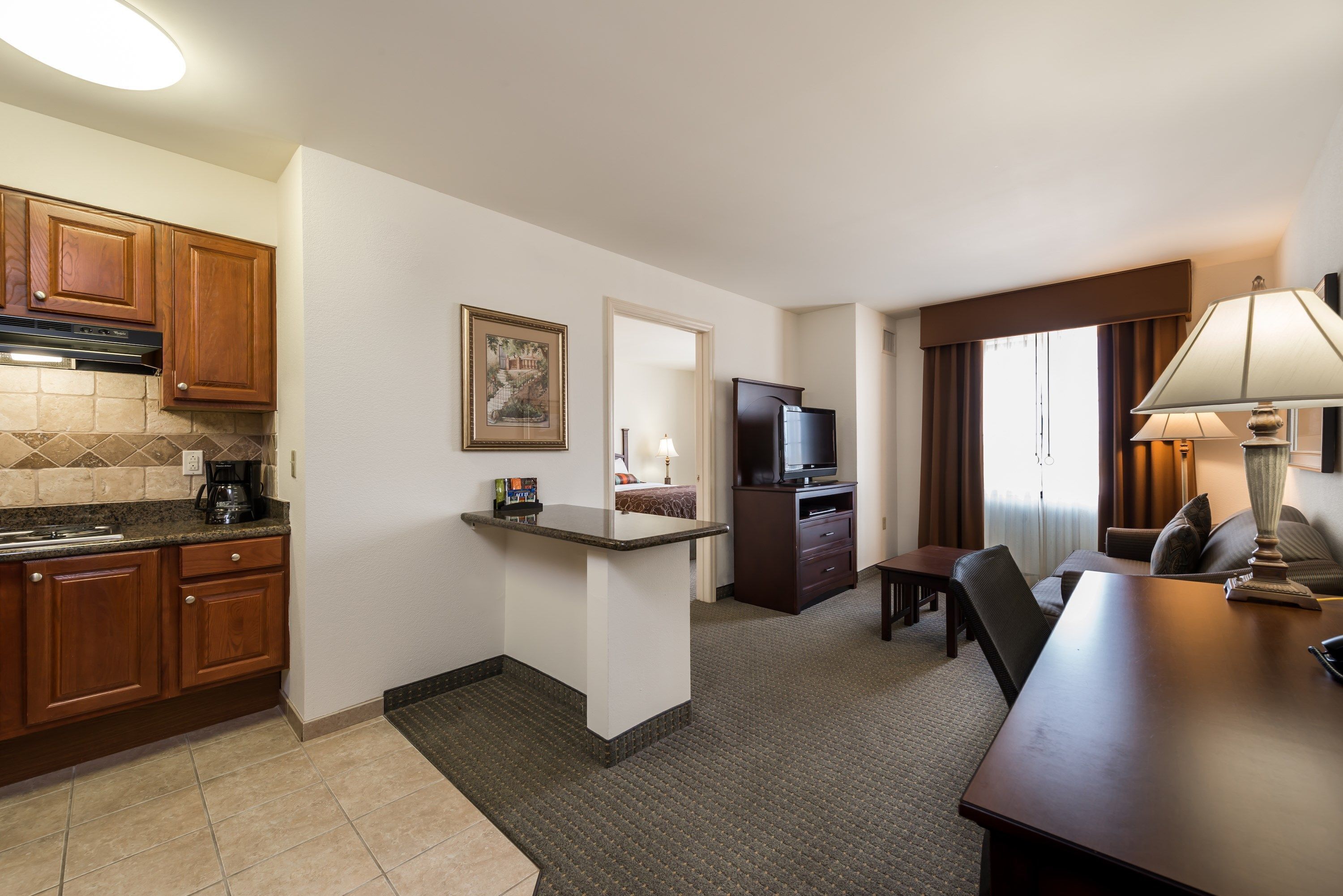 A compact hotel room with a kitchenette, a dining area, and a seating space.