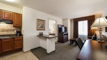 A compact hotel room with a kitchenette, a dining area, and a seating space.