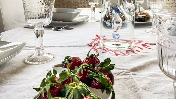 A dining table set with clear glassware, a bowl of fresh strawberries, and a pitcher of water.