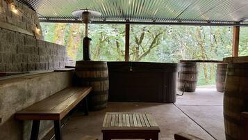 An outdoor patio with wooden benches and tables, a stone wall, and a view of trees.