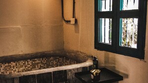 Une salle de bain avec une baignoire, un petit lavabo, une fenêtre avec des volets bleus et une serviette sur le sol.