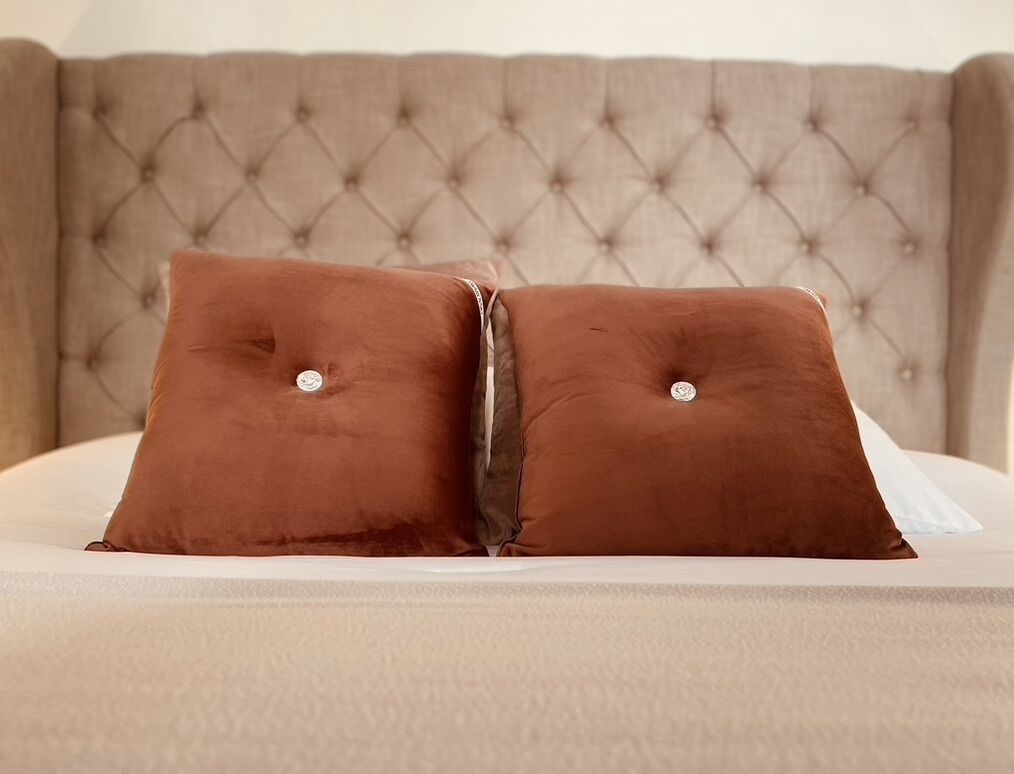 Cama com duas almofadas castanhas e cabeceira estofada.
