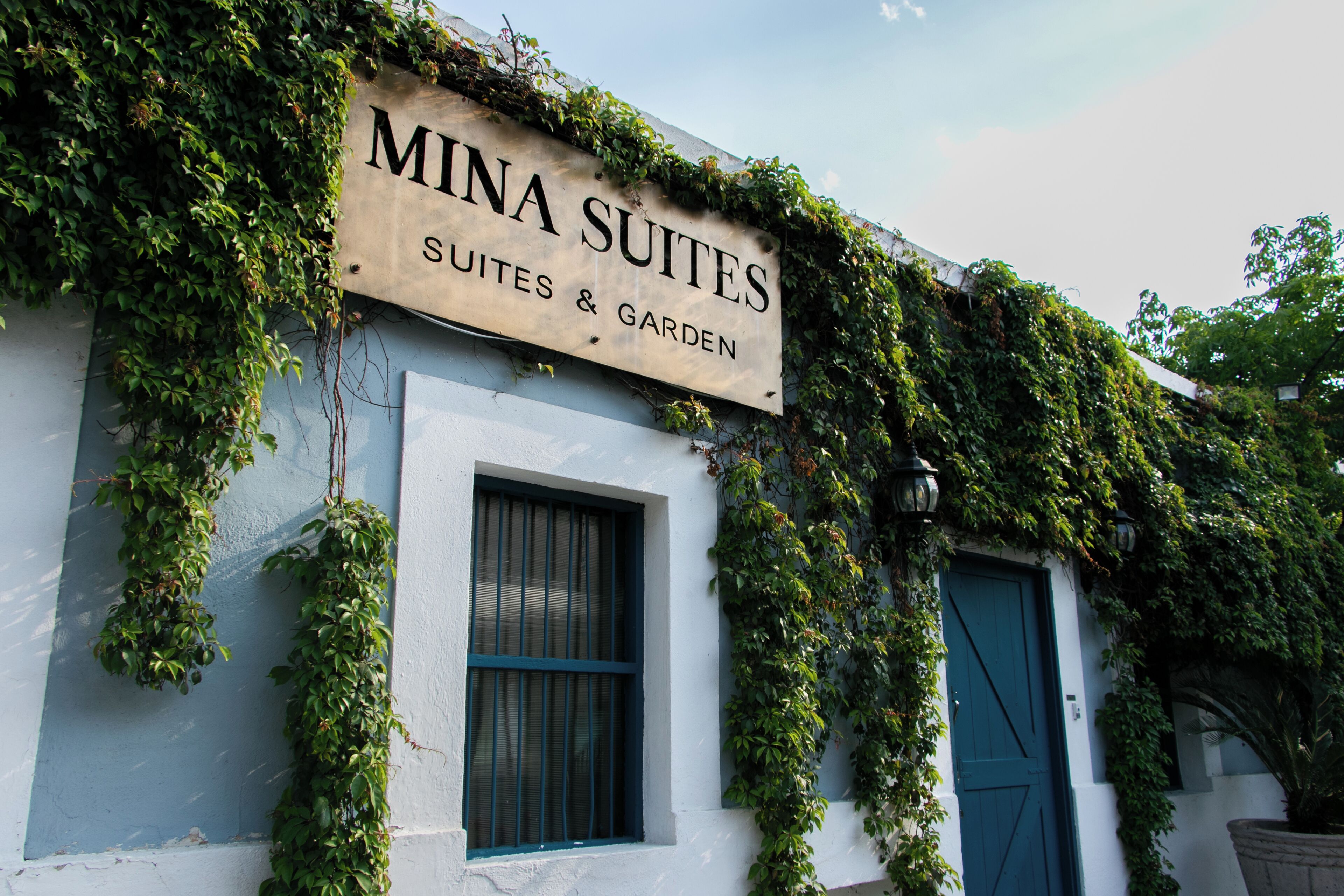 Un immeuble avec une enseigne indiquant « Mina Suites » et un jardin.
