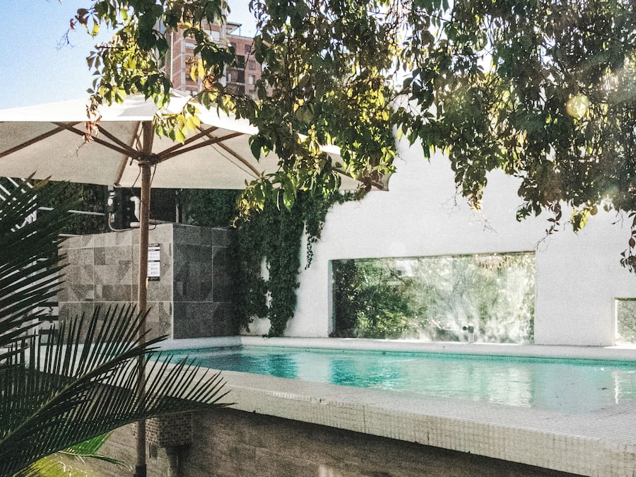 A swimming pool with a tiled edge, surrounded by greenery and a stone wall.