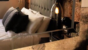 Une chambre à coucher avec une tête de lit capitonnée, un lit avec des oreillers, une table de chevet, un miroir et une suspension.