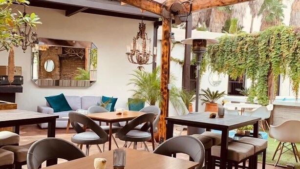 Un espace de restauration en plein air avec des tables et des chaises en bois, un lustre suspendu et un mur de pierre agrémenté d’un miroir.