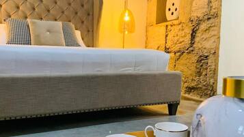 A hotel room with a tufted headboard bed, a stone accent wall, a hanging light fixture, and a table with two cups and a vase.