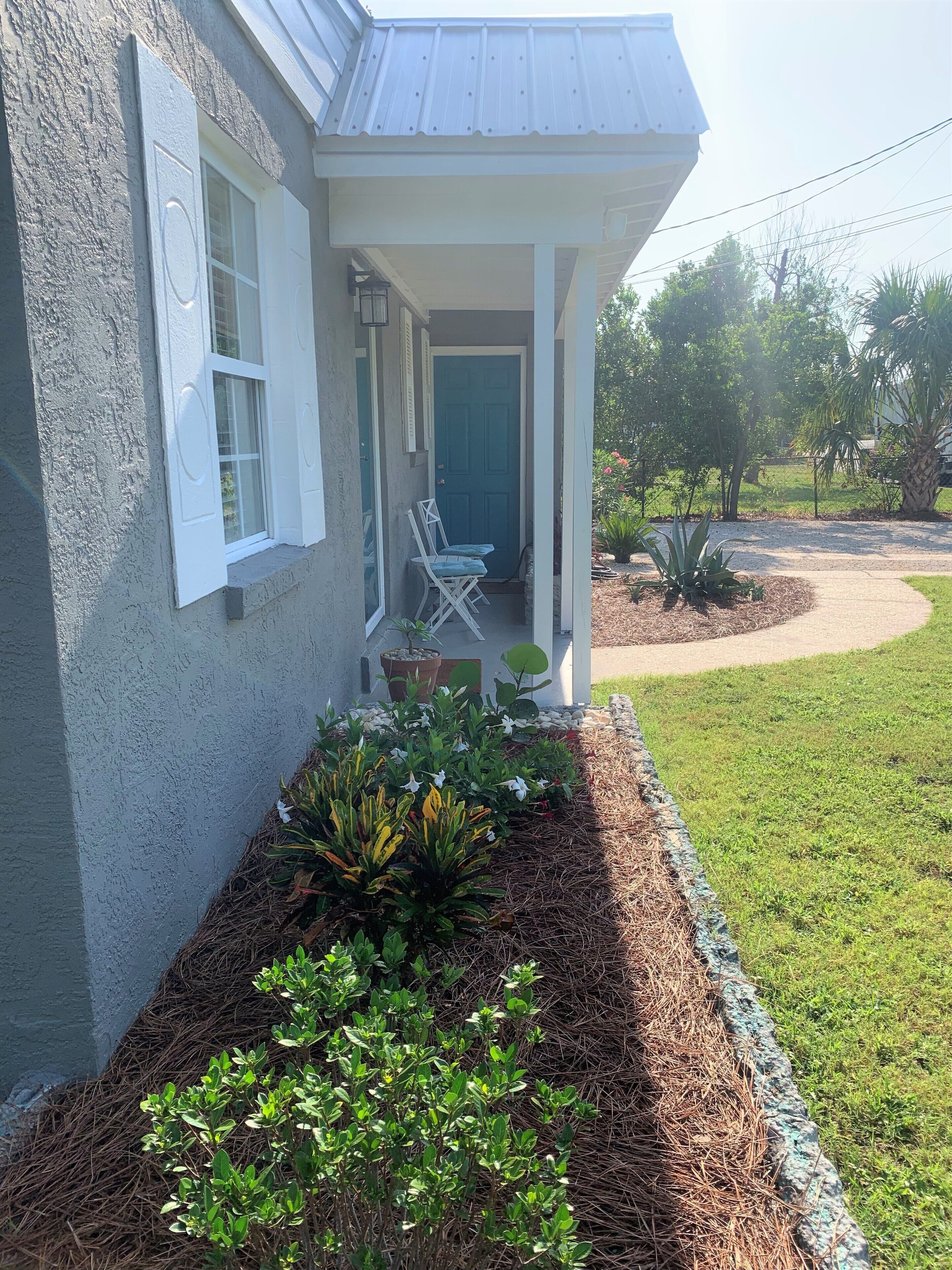 A house with a covered porch, a small garden with plants and mulch, and a clear sky.