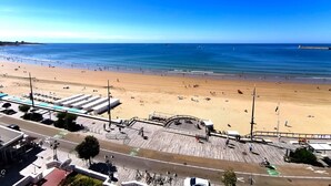 Une plage avec une promenade en bord de mer, un espace de stationnement et une vue sur l’océan.
