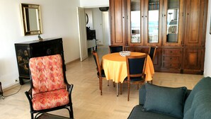 Un salon comprenant un canapé, une table à manger avec des chaises, un meuble avec des livres et un miroir au mur.