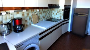Une cuisine compacte avec des meubles blancs, un lave-linge Bosch, une machine à café et un réfrigérateur.