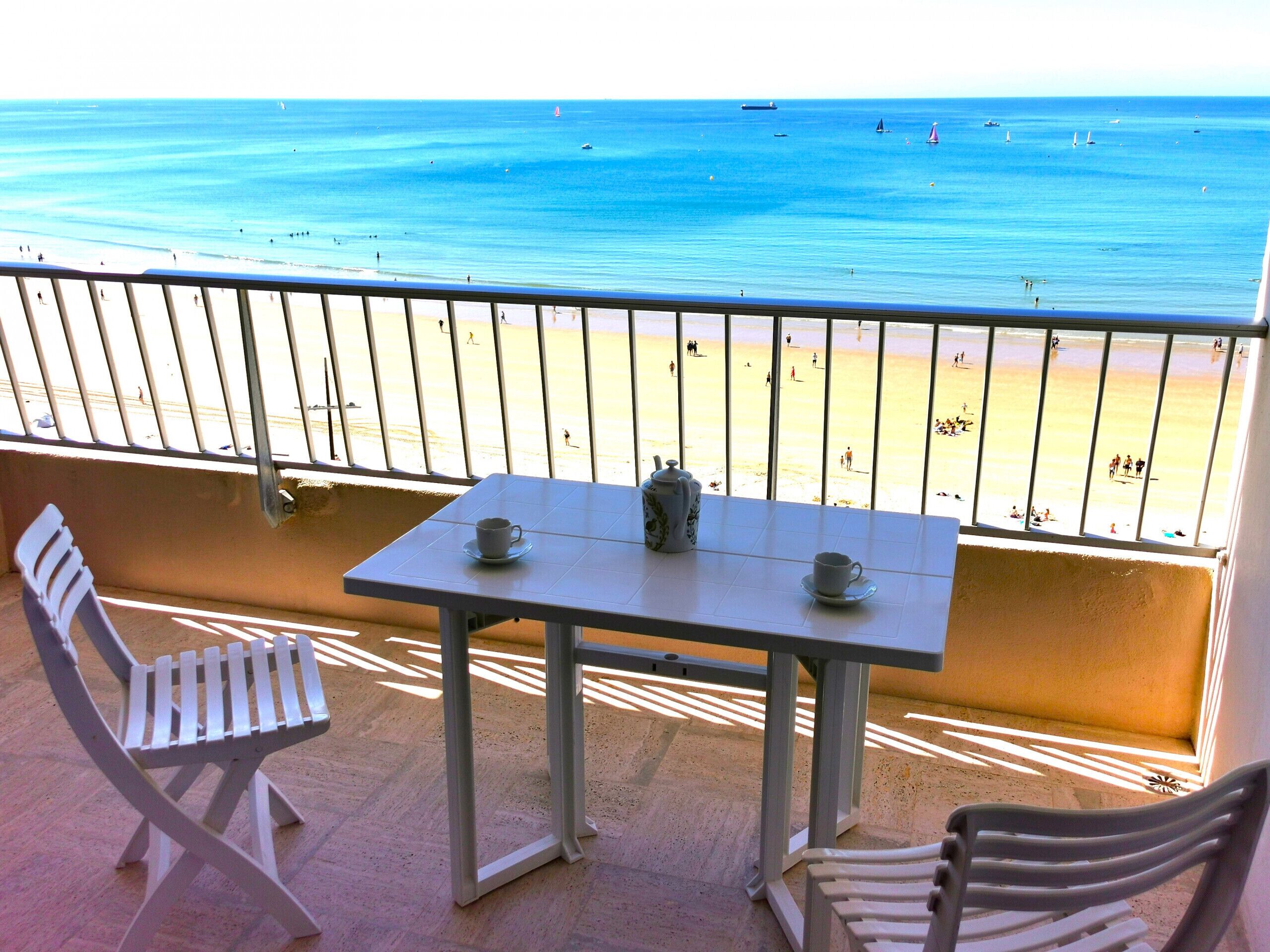 A balcony with a table and chairs overlooking a beach.