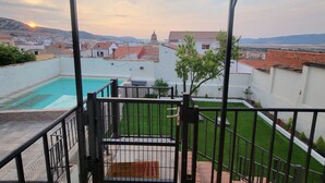 Un balcon avec une piscine, une vue sur une ville avec ses bâtiments et son église, et un ciel dégagé.