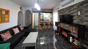 Un salon moderne avec un canapé noir, une table basse blanche, un téléviseur et une cheminée.