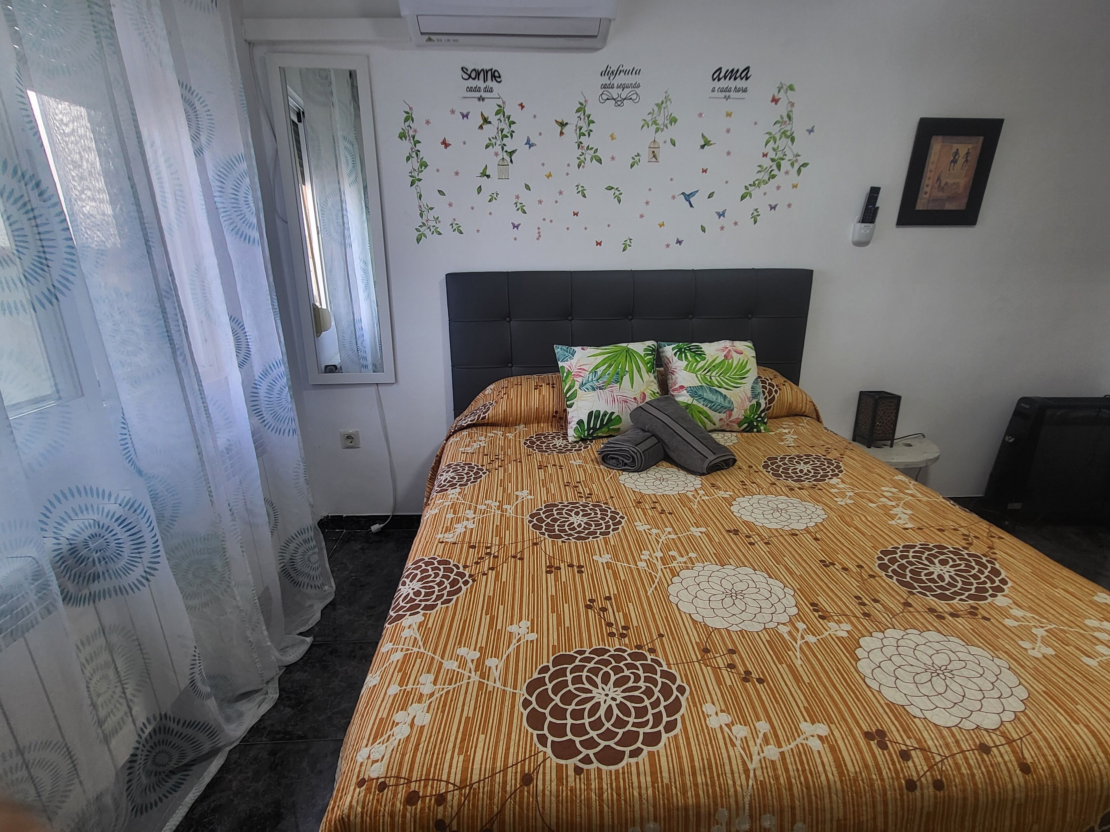 A bedroom with a bed, a window with curtains, a wall with decorative stickers, and a framed picture.