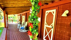 Une terrasse en bois agrémentée d’une plante suspendue, de fauteuils à bascule et d’une table recouverte d’une nappe à motifs.