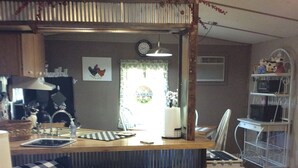 Une cuisine avec un îlot central en bois, des tabourets de bar, un réfrigérateur et un four à micro-ondes placés sur une étagère en métal.
