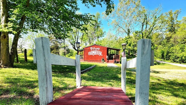 Une ferme rouge, avec une pancarte accueillante, entourée d’une végétation luxuriante et d’arbres.