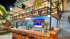 A bar area with a wooden deck, a counter with stools, and shelves with bottles. - Hotel Coco Beach by Croma (Cartagena)