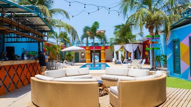 A poolside area with wicker furniture, a bar, and a colorful building. - Hotel Coco Beach by Croma (Cartagena)