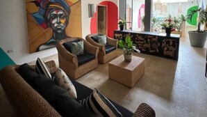 A modern living room with wicker furniture, a large abstract painting, and a view of a courtyard with plants. - Hotel Coco Beach by Croma (Cartagena)