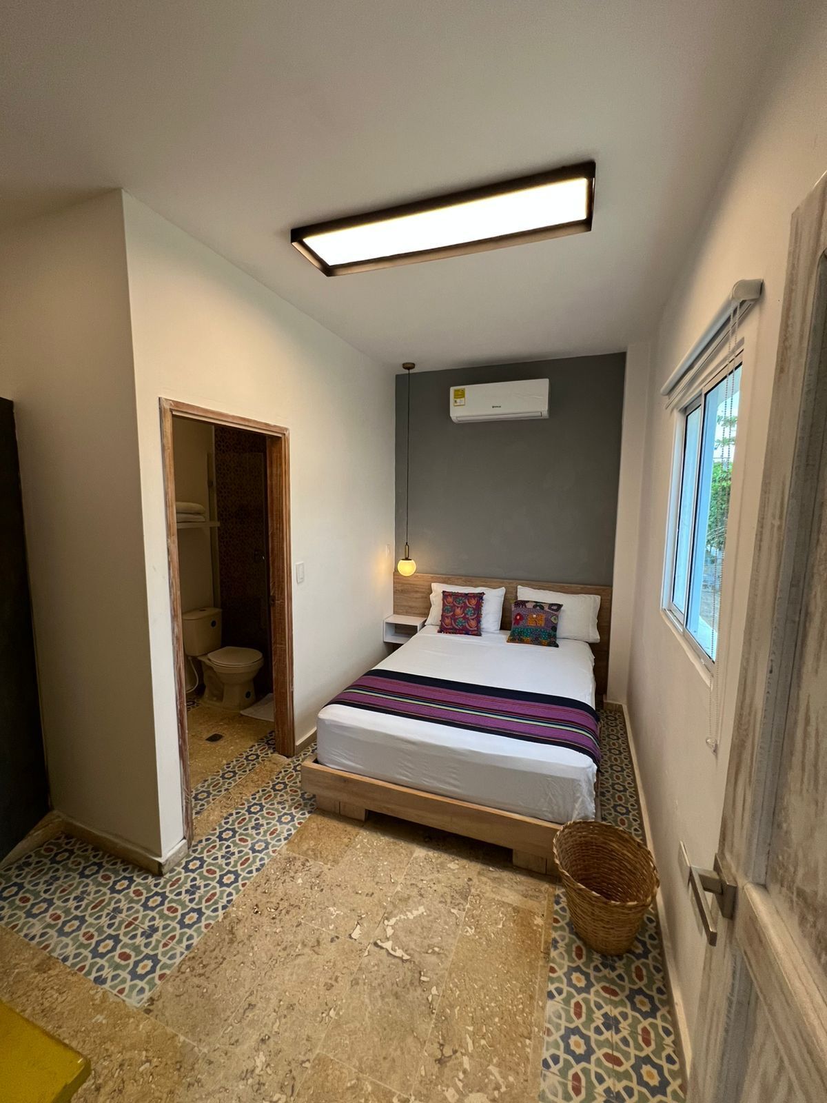 A bedroom with a bed, a bedside table, an air conditioning unit, a window, and a patterned floor.