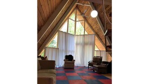 Un acogedor dormitorio en el ático, con techo inclinado, suelo a cuadros y un ventanal con cortinas.