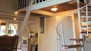Un loft amplio con techo alto, vigas de madera a la vista, una escalera blanca y un comedor con mesa y sillas.