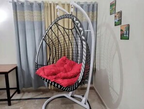 Relax in a hanging chair with a comfortable cushion, suspended from a sturdy frame, in front of a window with a view.