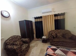 Ein Wohnzimmer mit gestreiften Sofas, einem schwarzen Kleiderschrank, einem kleinen Tisch und einer Wanduhr.