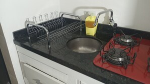 Una cucina con un lavello, un espositore per piatti, una bottiglia gialla e un fornello rosso.