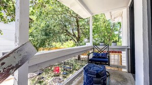 A covered balcony with a view of trees, a blue cushioned chair, and a patterned ottoman. - The Charmer, Super Close to UT + Downtown (Austin)